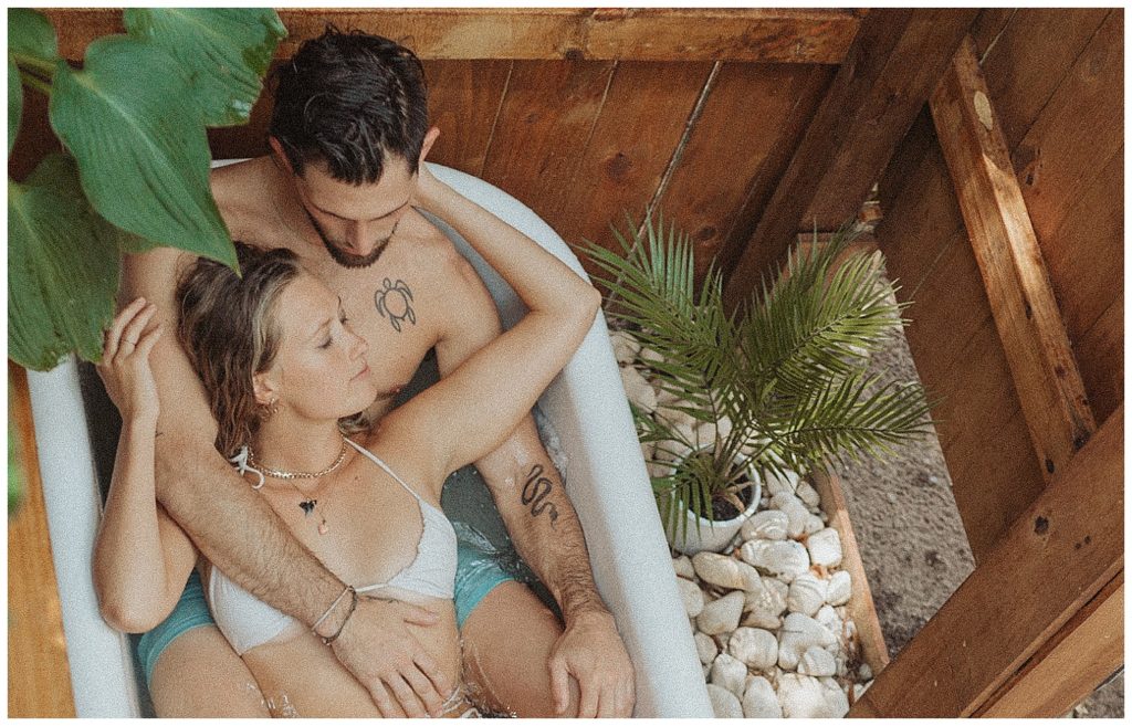 a couple laying in an outdoor bathtub with boho vibes with plants and rocks around them in florida