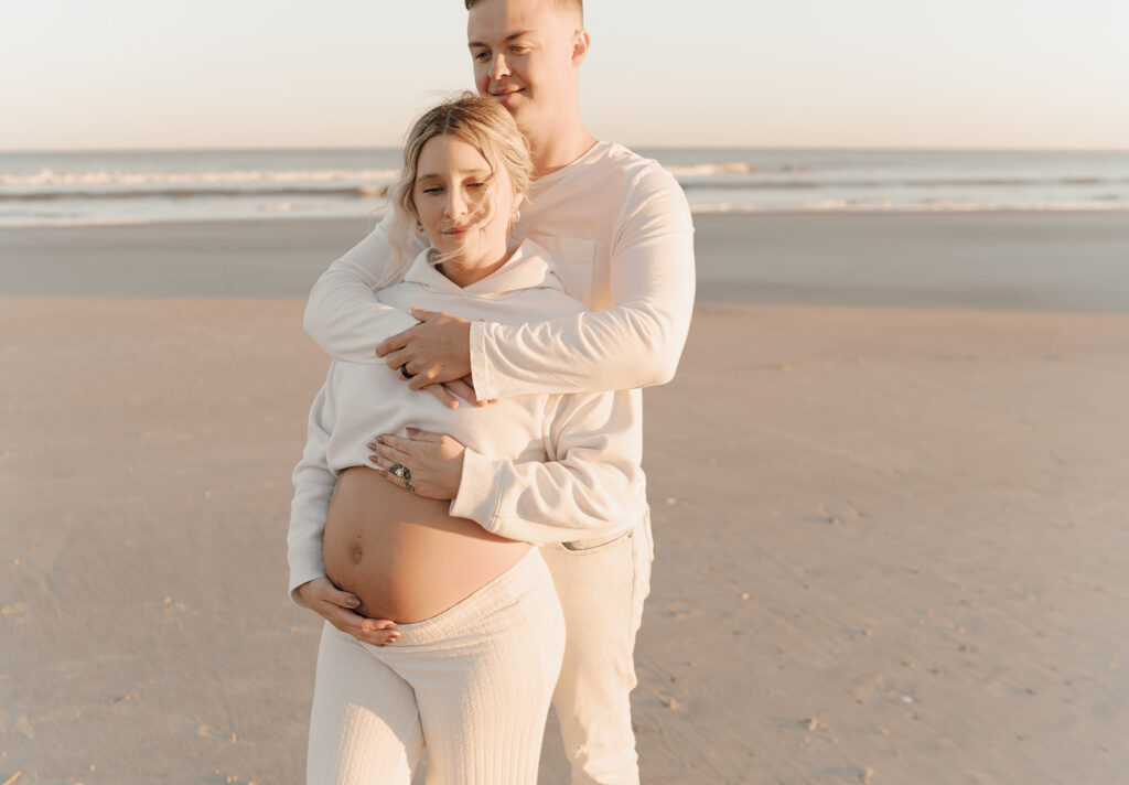 Couple walking on the beach holding baby bump