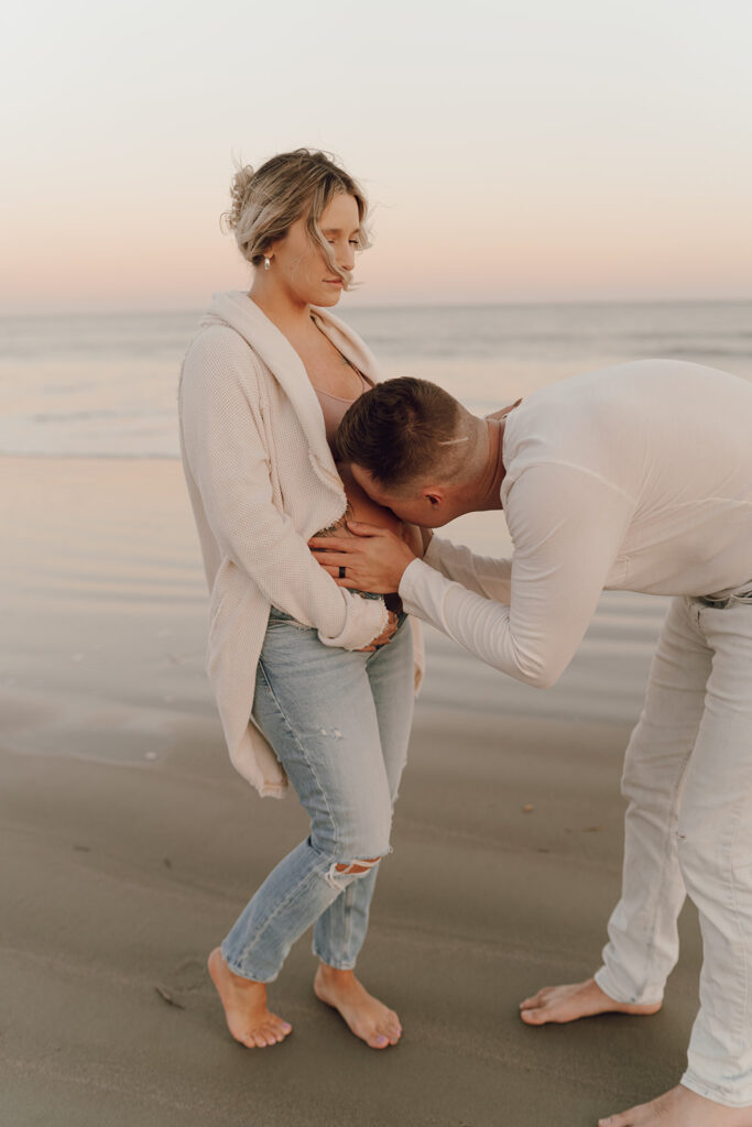 Dad to be kissing baby bump during beach maternity shoot