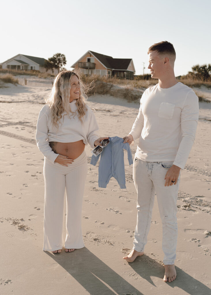 Couple holding baby clothes and baby scan picture at maternity shoot