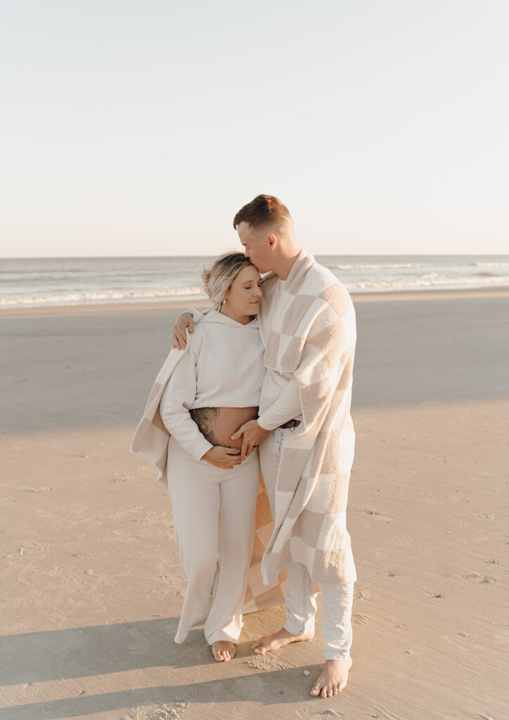 Couple walking on the beach holding baby bump during maternity shoot