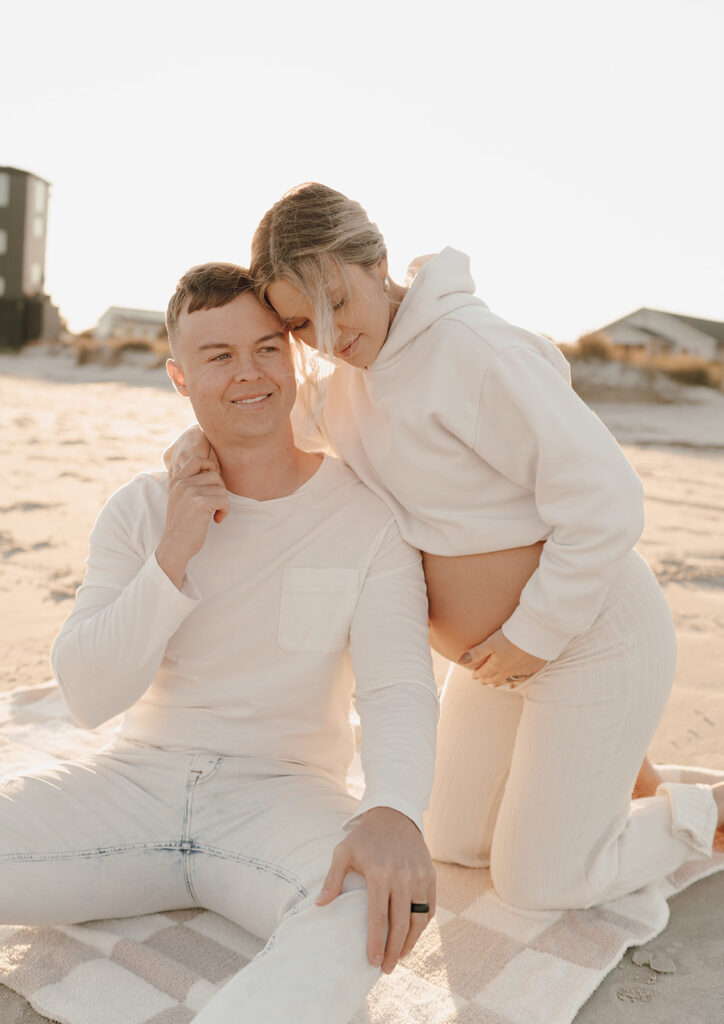 Couple laying on the beach holding baby bump during maternity shoot