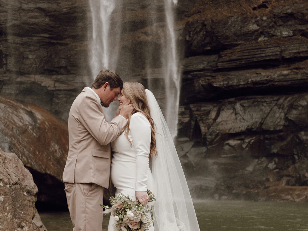 bride and groom posing for destination elopement photos under waterfall
