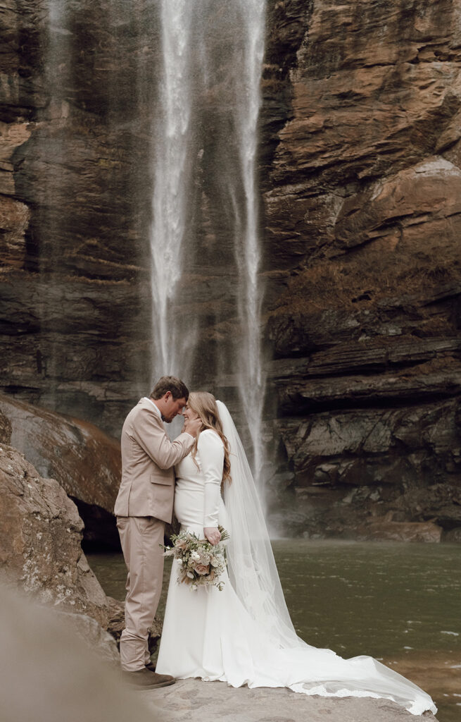 bride and groom posing for destination elopement photos under waterfall
