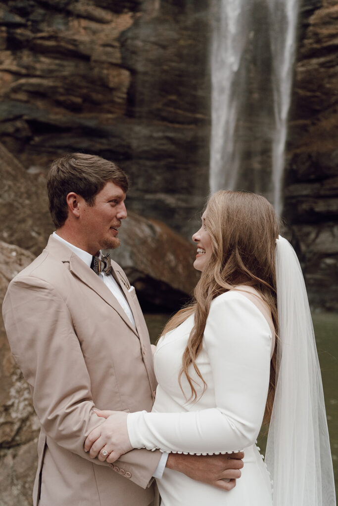 bride and groom smiling under waterfall