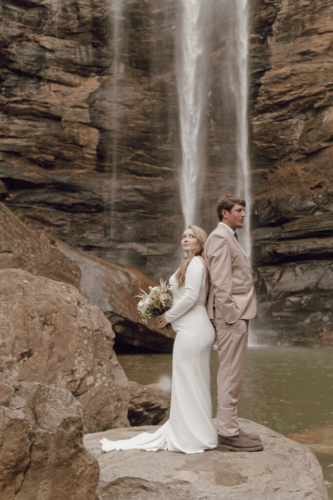 couple standing back to back under waterfall for elopement