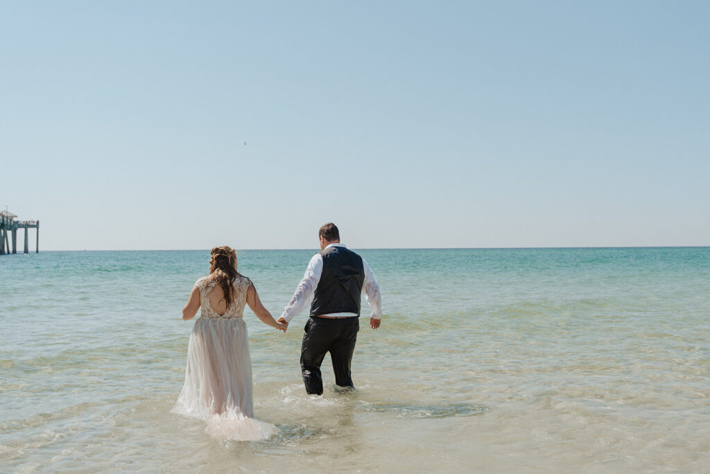 bride and groom holding hands and walking on the shoreline