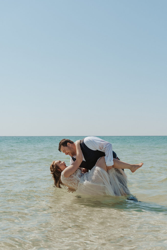 bride and groom dip pose for beach wedding in the water