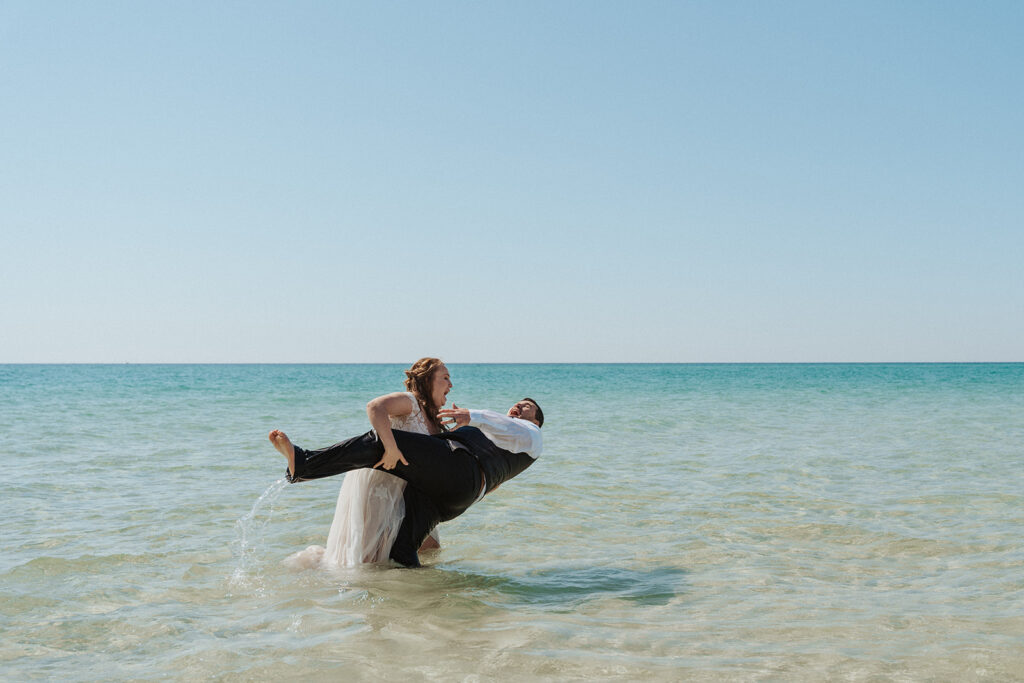 bride and groom having fun in the ocean for beach wedding photos