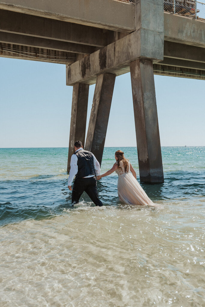 bride and groom holding hands and walking in the water