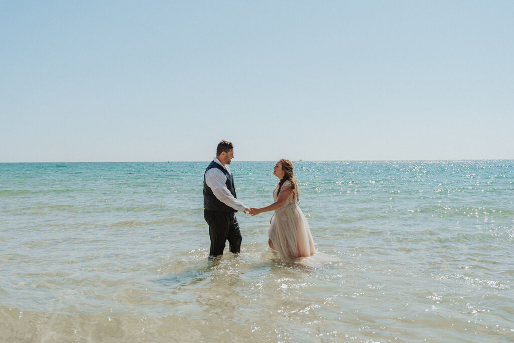 couple smiling and holding hands in the water during wedding