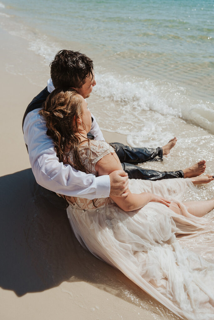 couple sitting in the water on the beach for trash the dress photoshoot