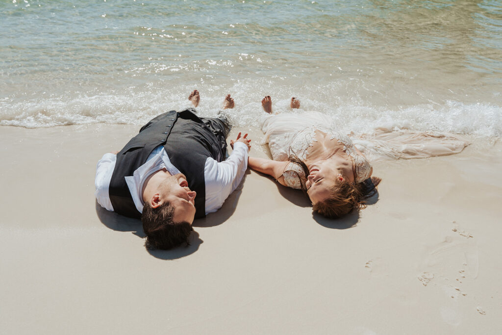 bride and groom laying on the sand for trash the dress photoshoot