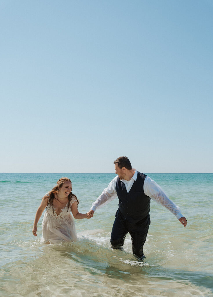 couple smiling and holding hands in the water during wedding