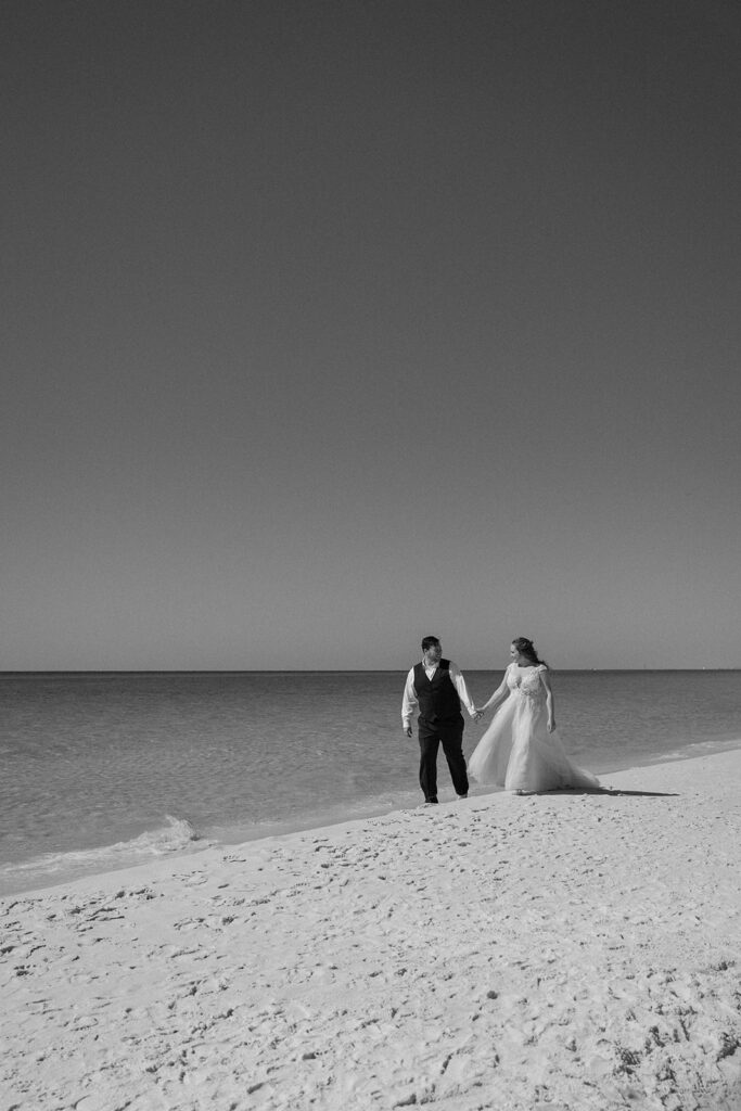 bride and groom holding hands and walking on beach