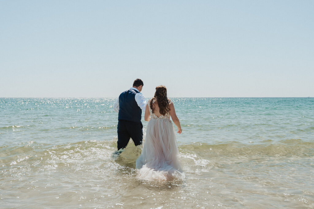 bride and groom walking in the water on the beach