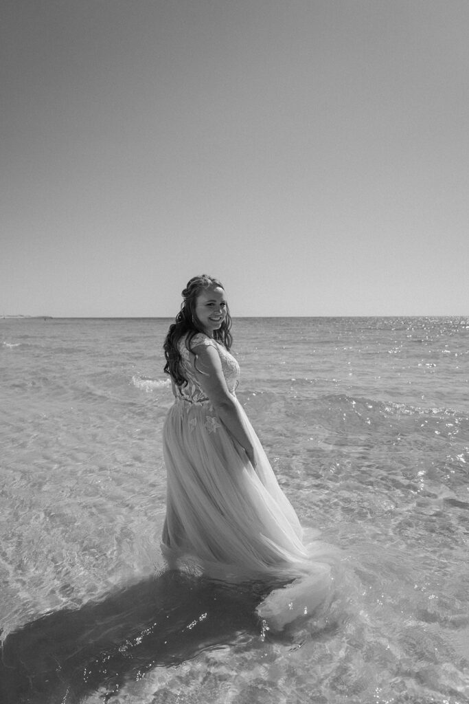 bride smiling in wedding dress in the ocean
