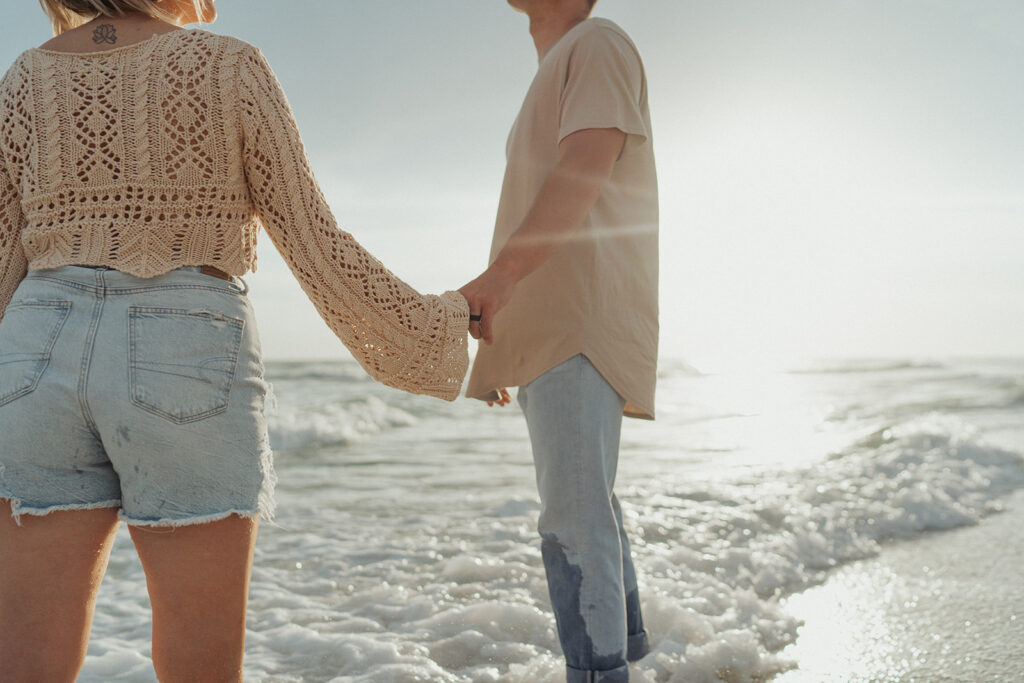 couple holding hands and smiling on the beach for engagement session