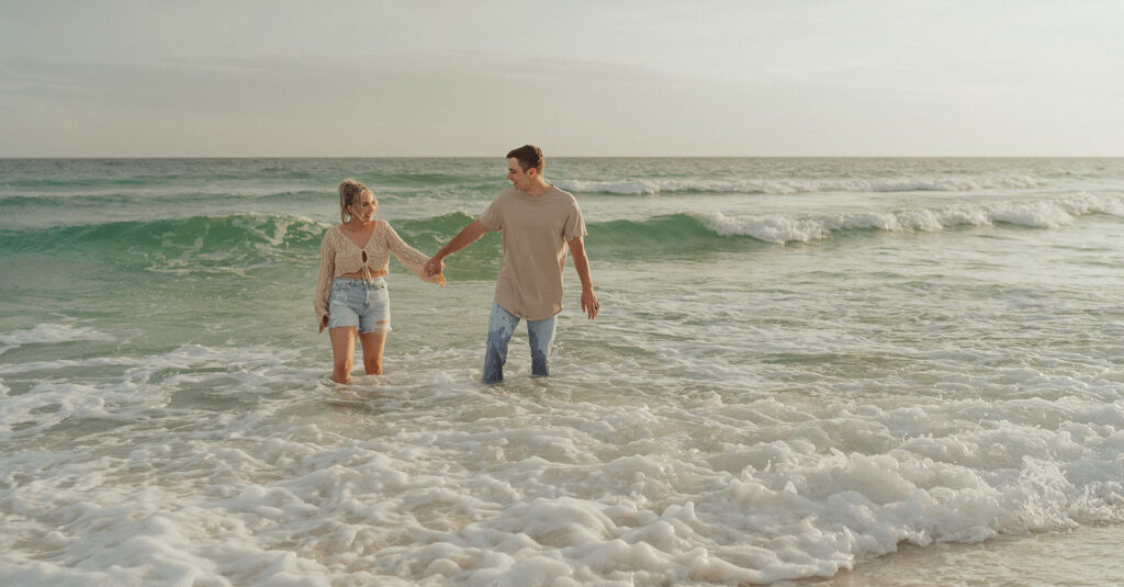 couple holding hands and smiling on the beach for engagement session