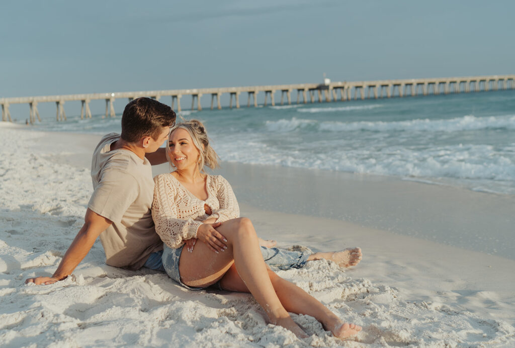 couple smiling and posing on the beach for engagement photos