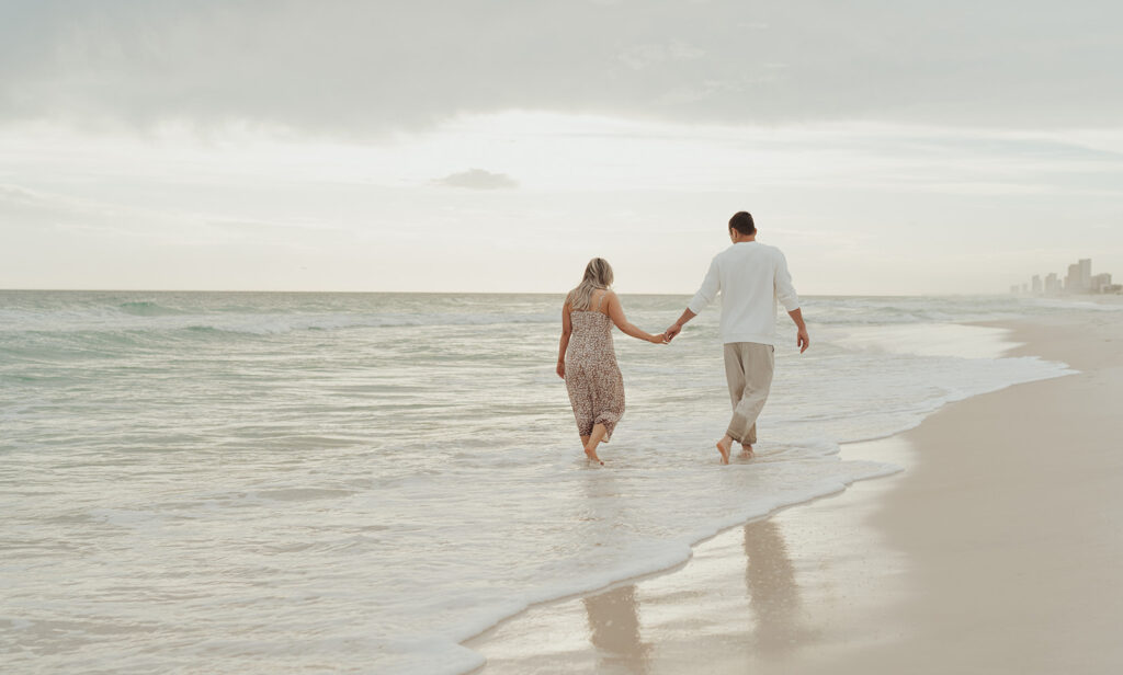 couple holding hands and walking on the shoreline 30A