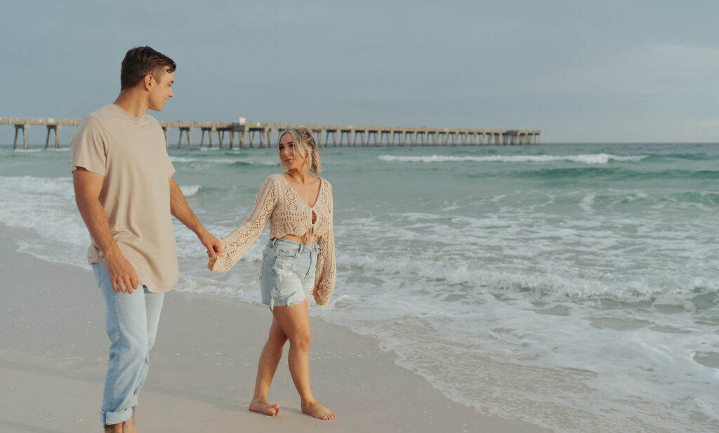 couple walking and holding hands on the beach during engagement photoshoot