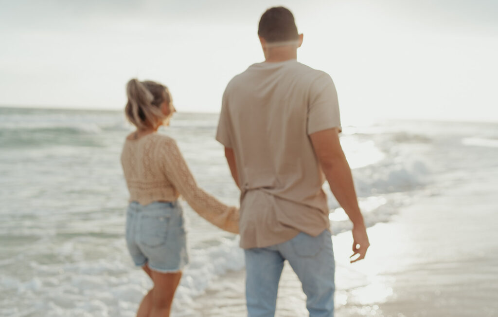 candid blurry beach engagement photos couple holding hands and walking
