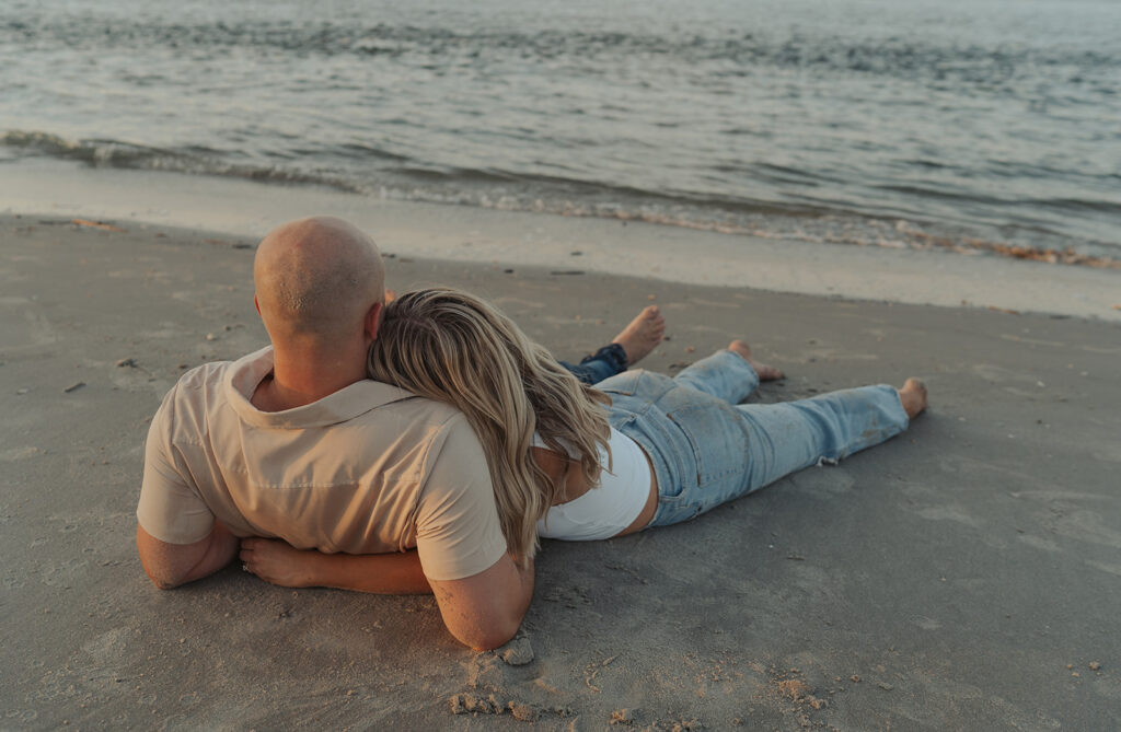 couple laying on the sand at folly beach south Carolina engagement photoshoot