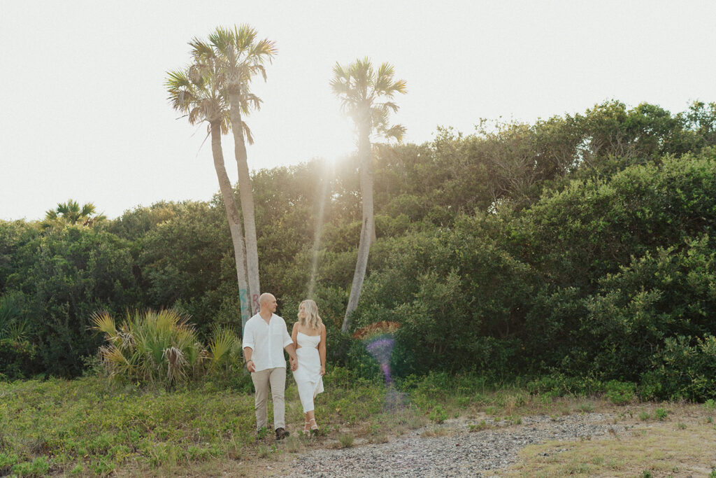 couple holding hands and walking in front of palm trees on folly beach