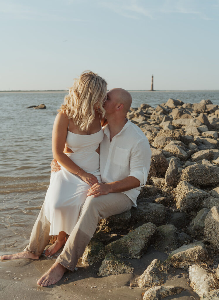 couple kissing and sitting on rocks at the beach during engagement session 