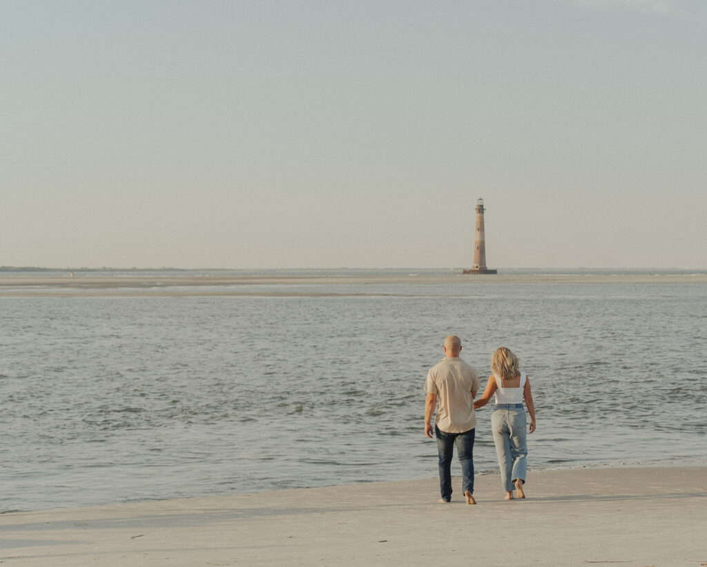 couple holding hands and walking along folly beach shoreline