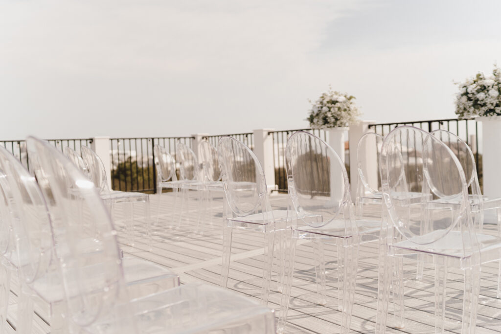 luxurious wedding ceremony with clear wedding chairs, white florals, on the rooftop in 30A