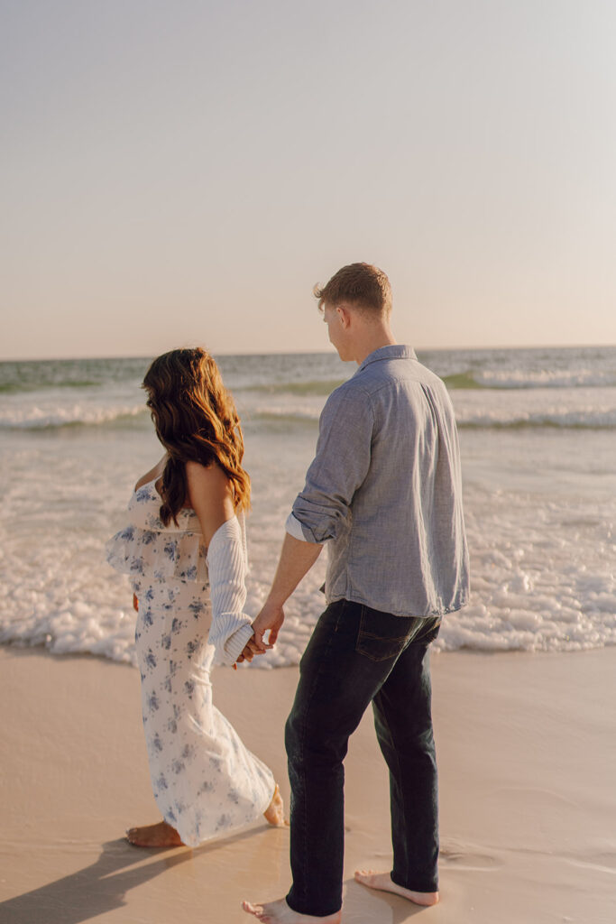 couple holding hands and walking on the beach during Grayton Beach Maternity Photoshoot