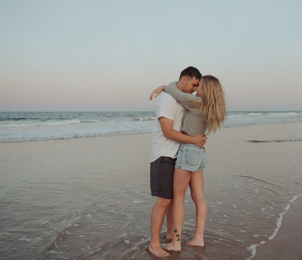 couple hugging and smiling at the beach for engagement session