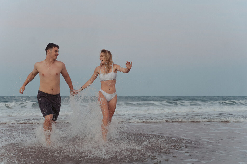 couple holding hands and running in the water at the beach