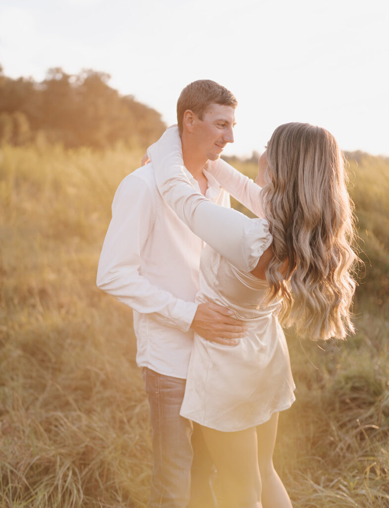couple smiling and hugging in field during engagement shoot