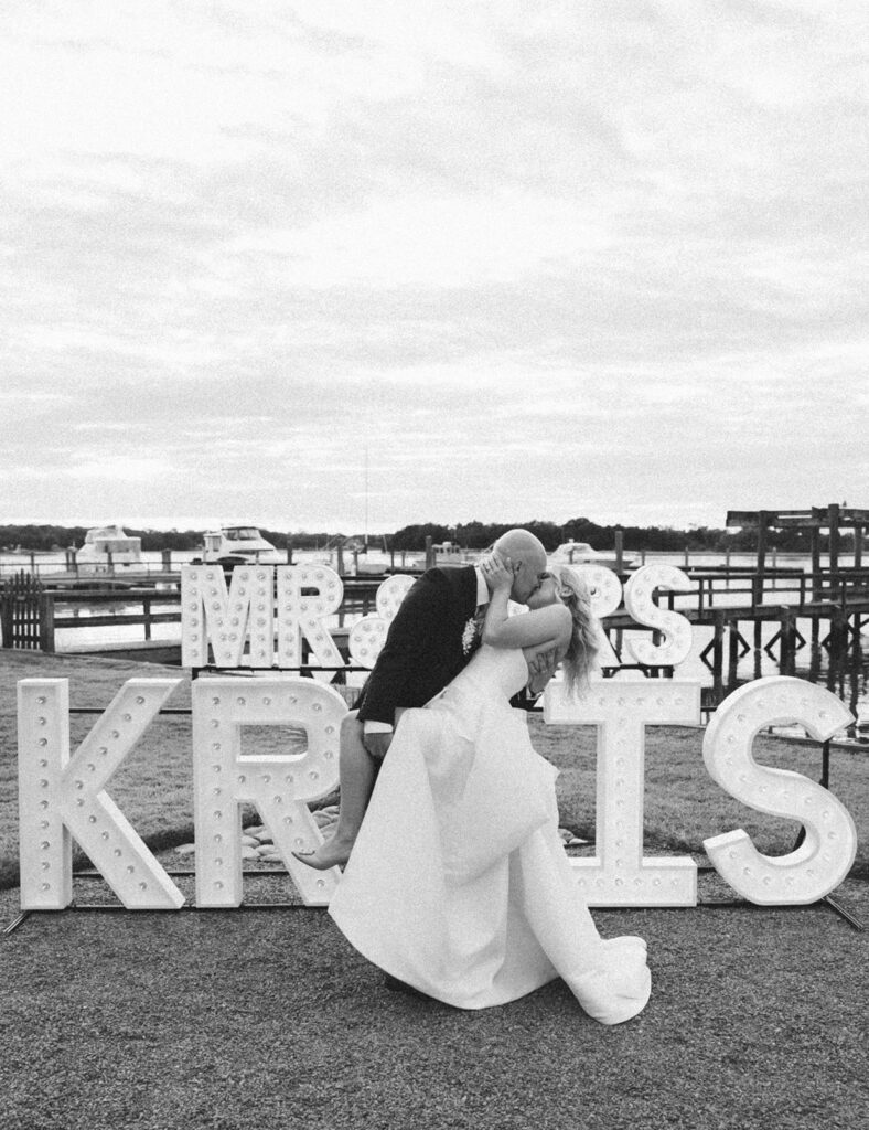 bride and groom dip kiss pose in front of letter sign