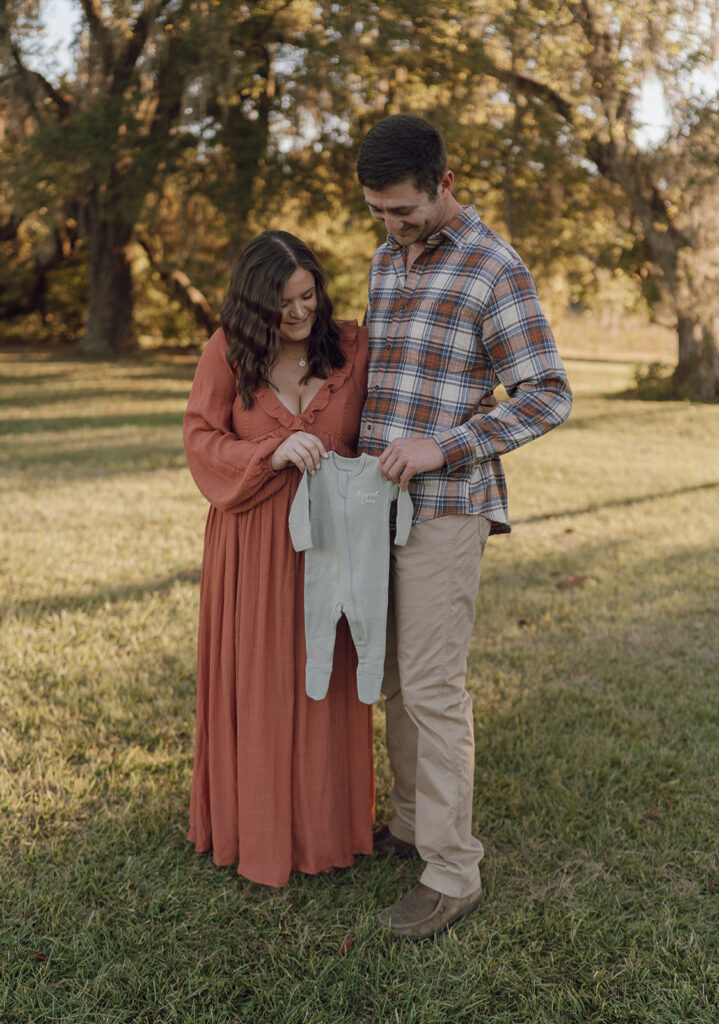 mom and dad holding up baby onesie during maternity photos couples session