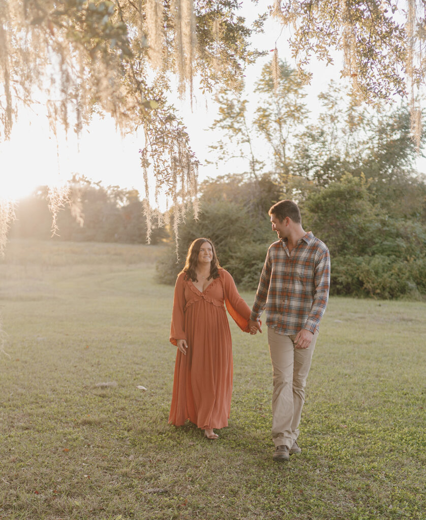 couple holding hands and walking under tree maternity session