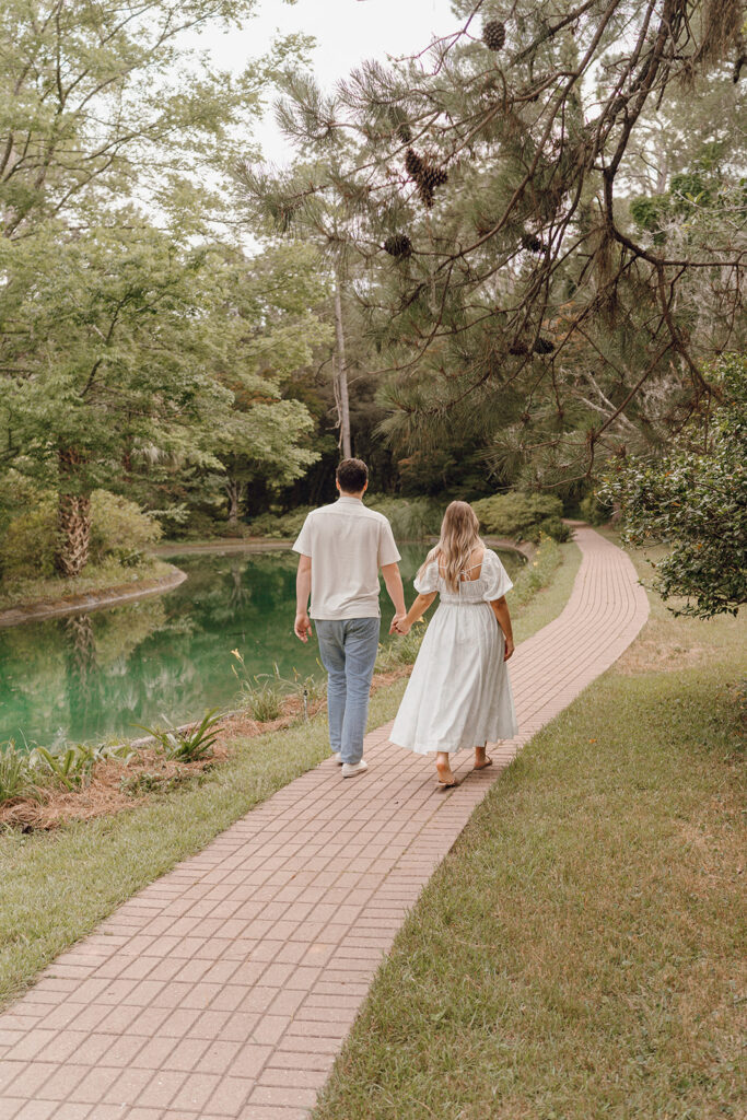 couple holding hands and walking on pathway in park