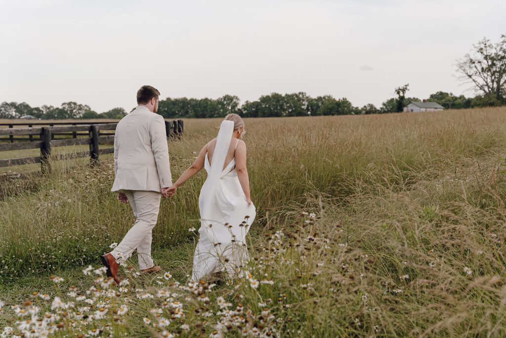 bride and groom holding hands and walking in a field