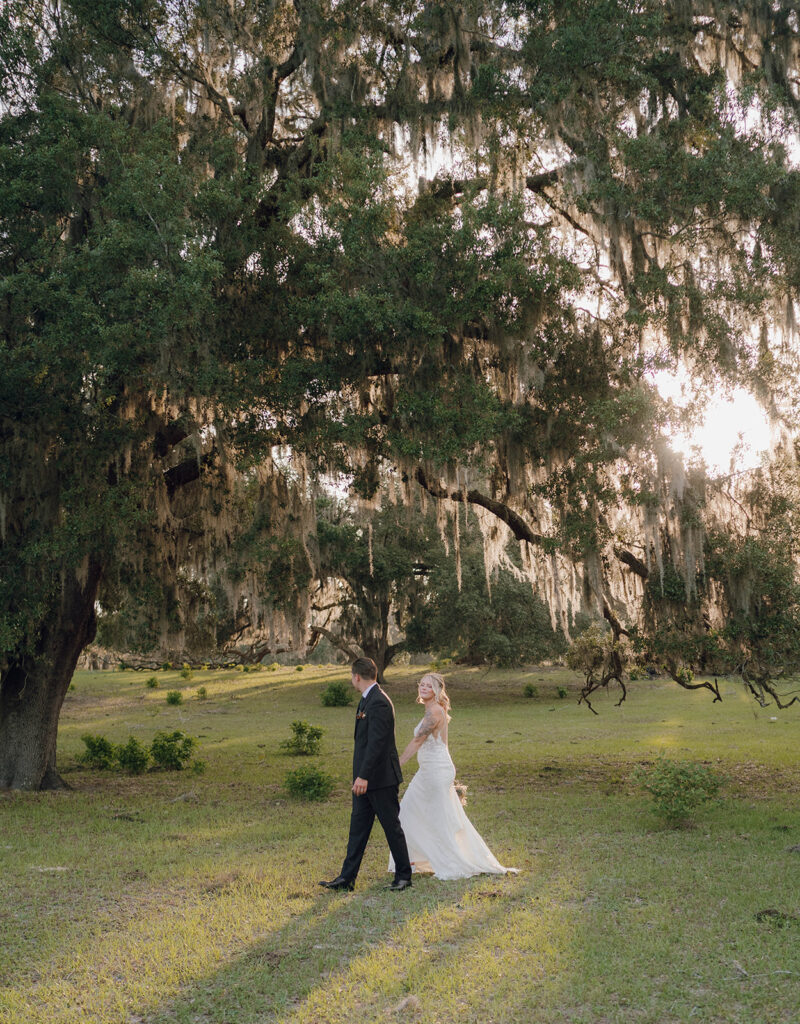 bride and groom holding hands walking under a willow tree