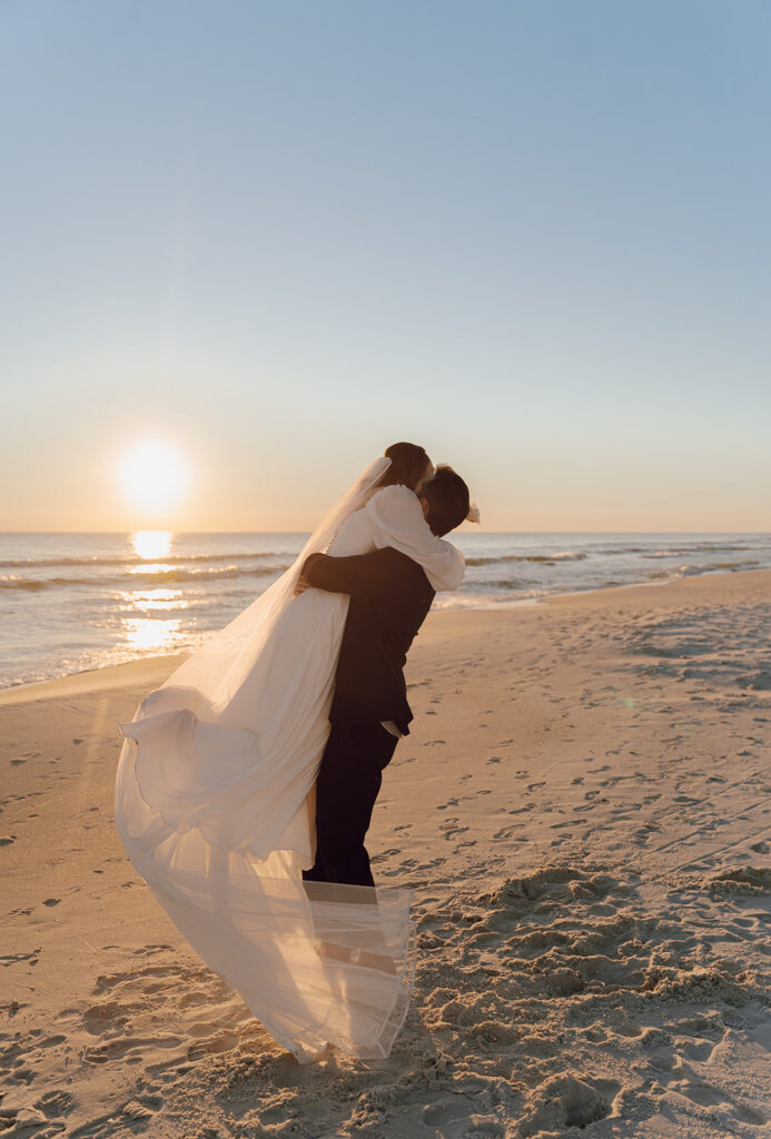 A groom holding his wife in the air after their 30A beach wedding.