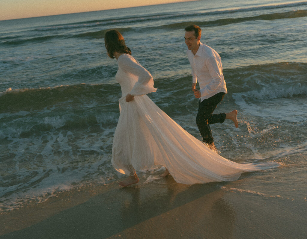 Groom playfully running after his bride alongside the ocean in 30A.