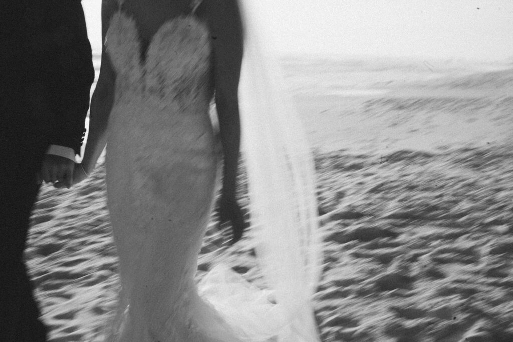 Newlyweds holding hands as they walk along the beach at sunset.