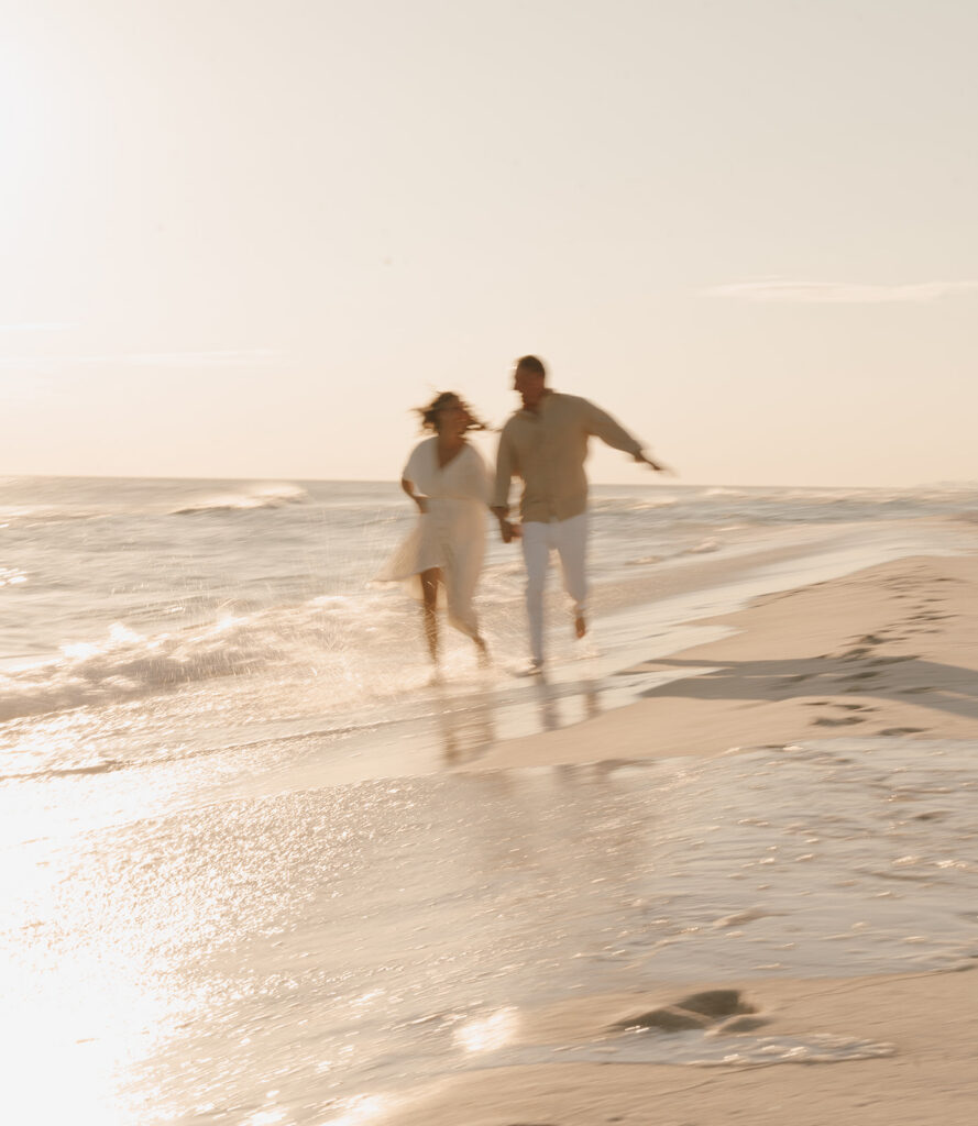 A blurred photo of a couple running hand in hand along the beach at sunset, with soft sunlight and gentle ocean waves—perfect inspiration for documentary style family pictures.