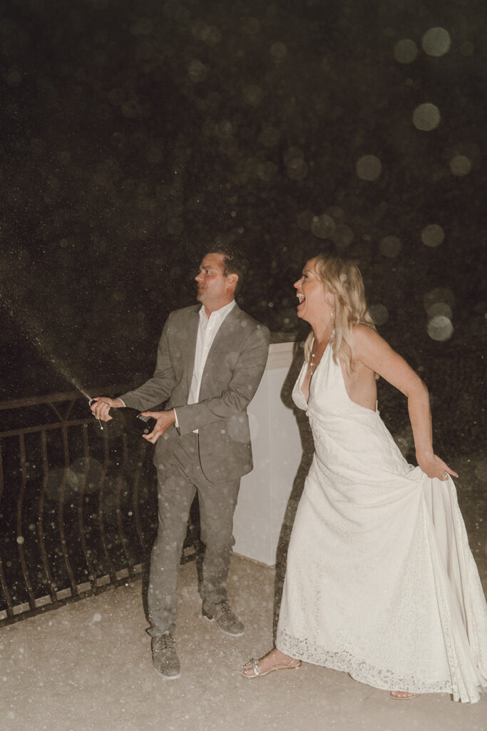 Groom spraying champagne while the bride cheers him on.