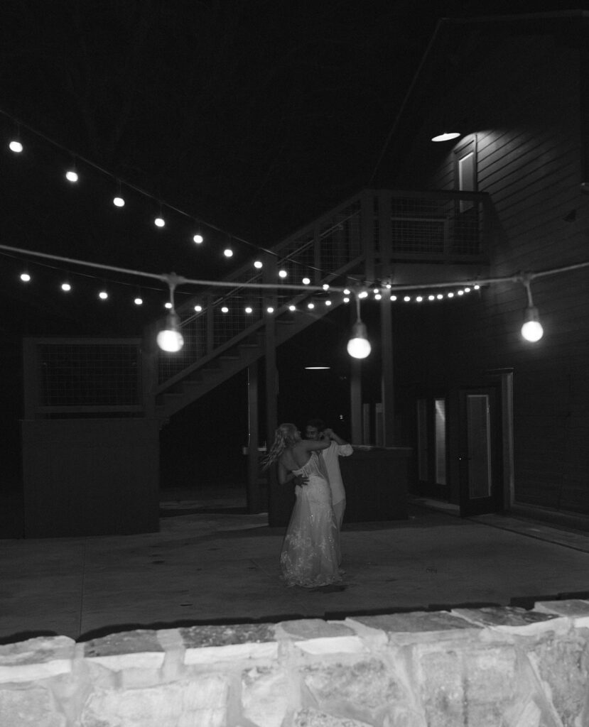 Candid wedding photos of the bride and groom slow dancing under string lights.