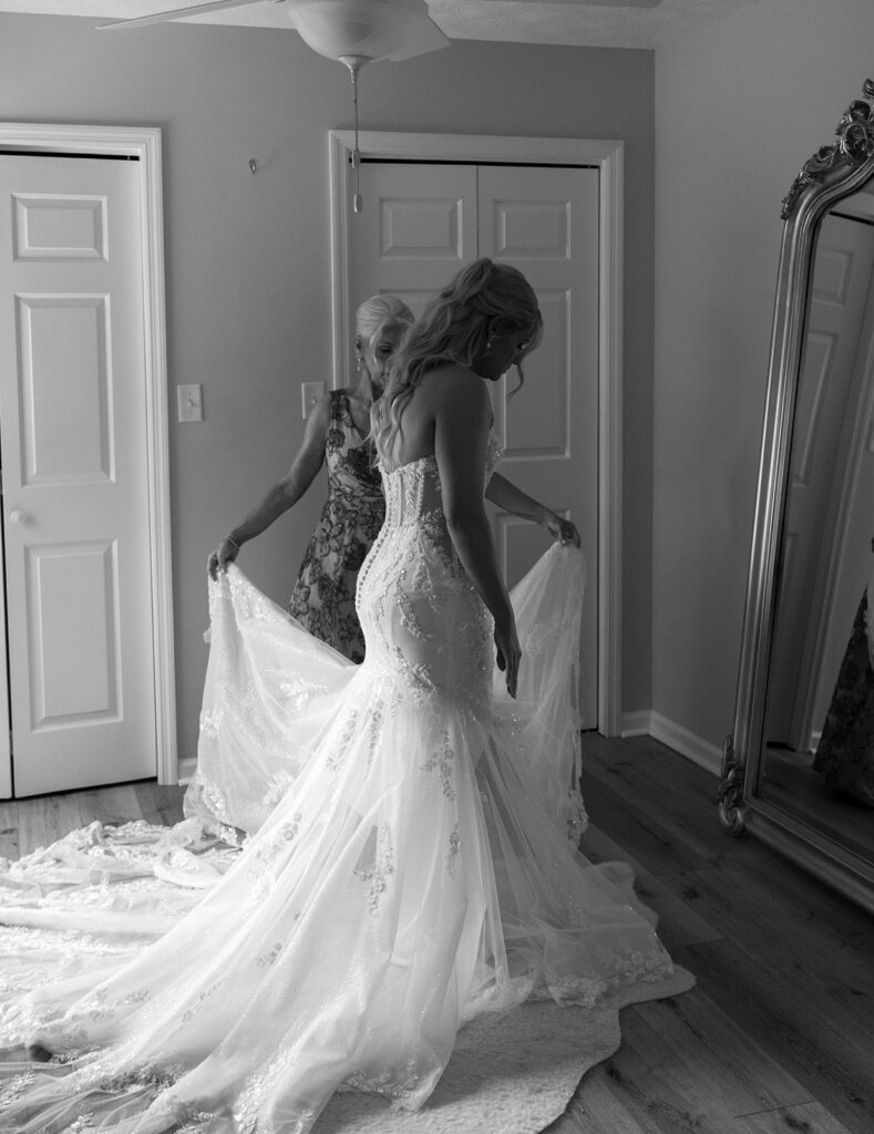 Mother of the bride helping the bride adjust her wedding gown.