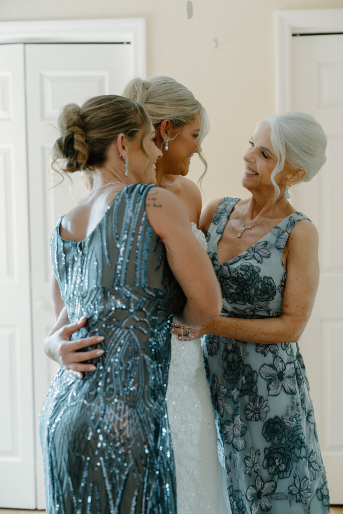 Mother and sister of the bride hugging the bride for candid wedding photos.